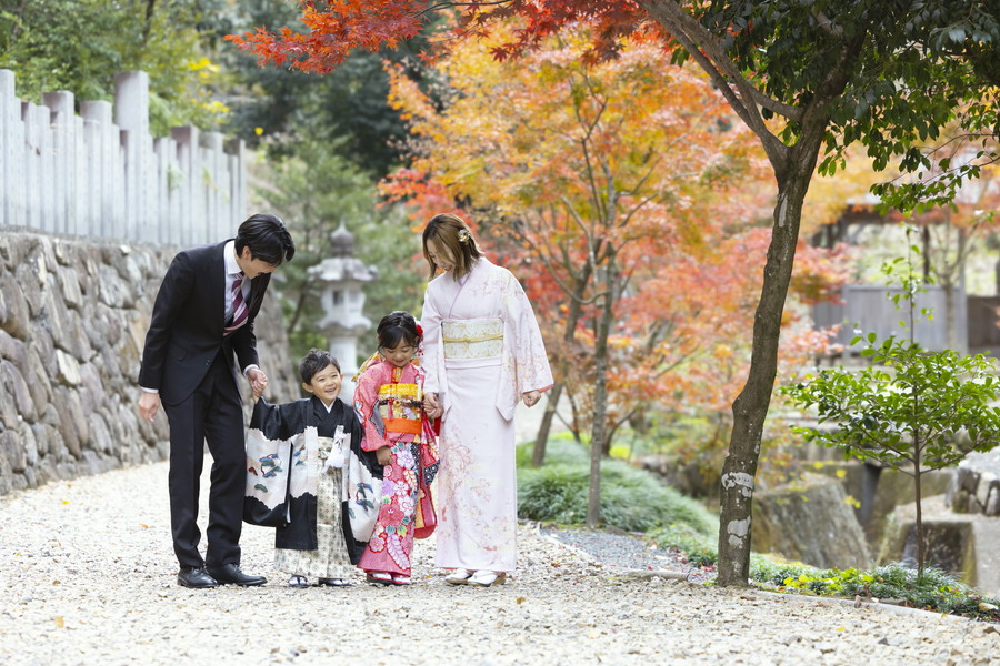 紅葉の中でお参りする七五三の家族